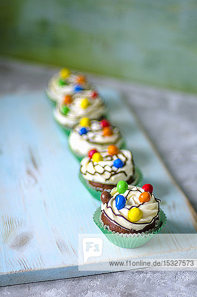 Schokoladen-Cupcakes in grünen Papierformen mit Buttercreme und bunten Bonbons