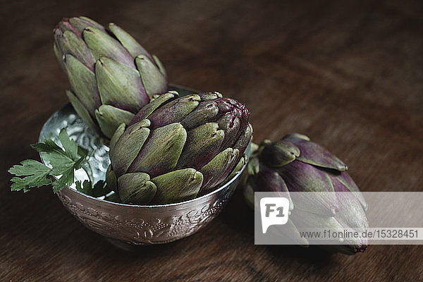 Three artichoke in a bowl over a wooden table