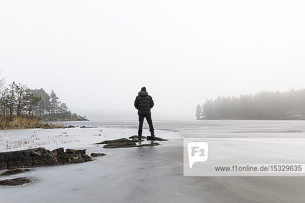 Mann auf Felsen im zugefrorenen See in Lotorp  Schweden