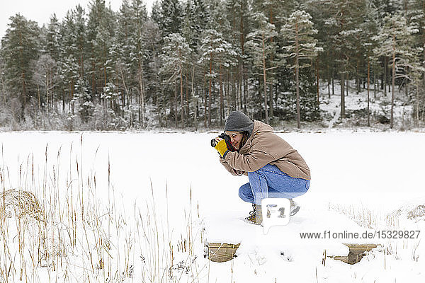 Hockende Frau beim Fotografieren im Schnee