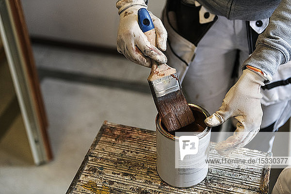 Hand of painter dipping paintbrush into paint can