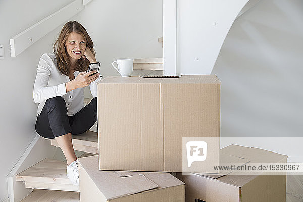 Woman sitting on staircase with smart phone and cardboard boxes