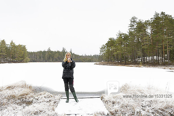 Junge Frau nimmt Selfie vor einem See im Schnee