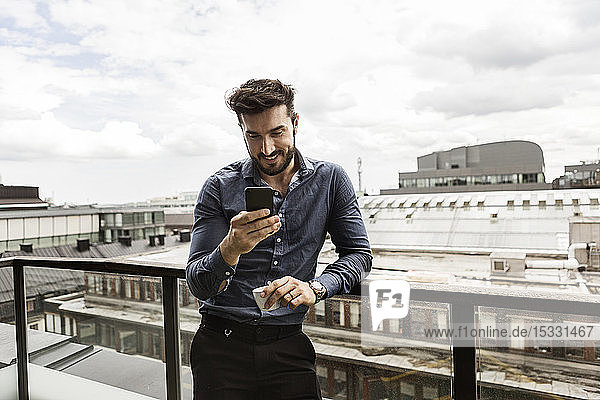 Junger Mann schaut auf dem Balkon auf sein Handy