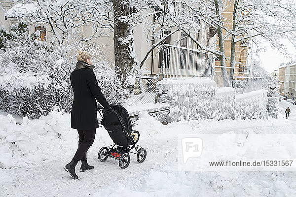 Young woman pushing a pram on a snowy city street
