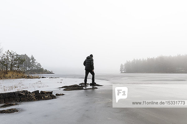 Mann auf Felsen im zugefrorenen See in Lotorp  Schweden