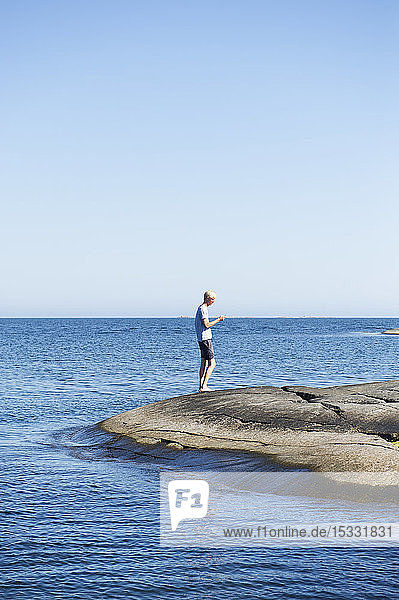 Junger Mann steht auf Felsen am Meer