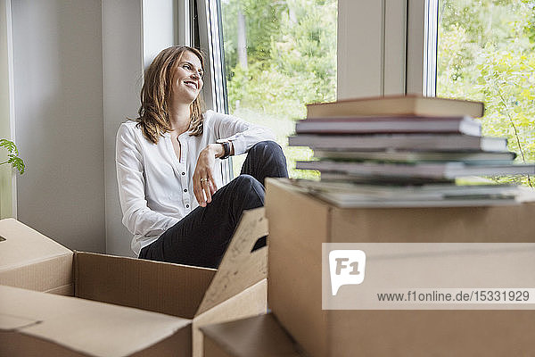 Woman sitting on window sill behind cardboard boxes