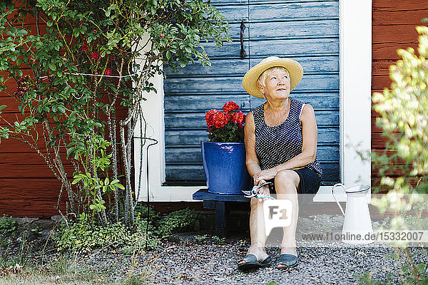 Senior woman sitting by flower pot in front of door