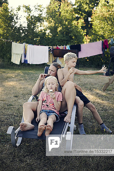 Mother with her son and daughter eating ice cream on sun lounger in back yard