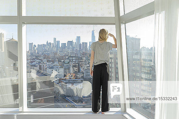 Teenage girl shielding eyes in front of city apartment window