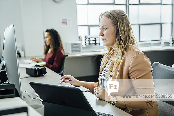 Frau mit Computer und digitalem Tablet im Büro