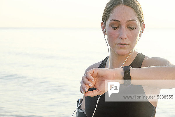 Frau mit Kopfhörern überprüft Armbanduhr am Strand