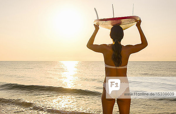 Frau mit Surfbrett auf dem Kopf am Strand bei Sonnenuntergang