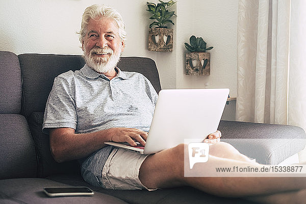 Lächelnder älterer Mann mit Laptop auf dem Sofa