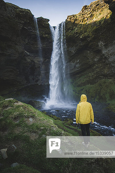 Mann mit gelbem Regenmantel am Kvernufoss-Wasserfall in Island