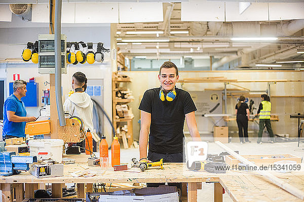 Portrait of confident young trainee standing at workbench at illuminated workplace