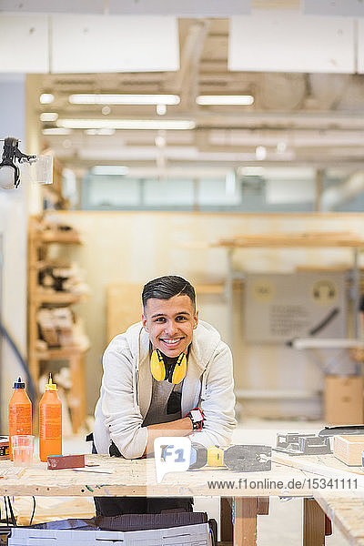 Portrait of smiling teenage trainee leaning on workbench at workshop