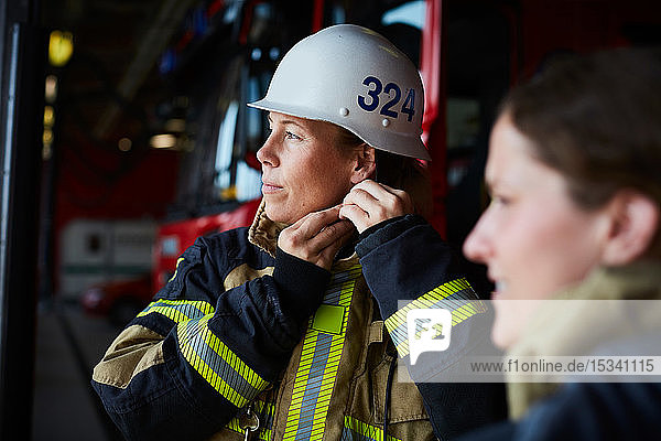 Weibliche Feuerwehrfrau mit Helm  während sie mit einem Mitarbeiter in der Feuerwache steht