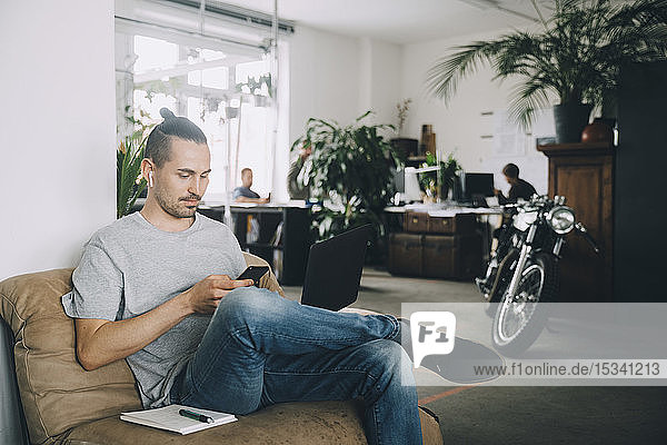 Selbstbewusster Geschäftsmann nutzt Technologien  während er im kreativen Büro sitzt