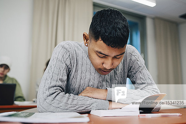 Teenage boy reading book while studying at table school