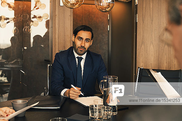 Portrait of confident mid adult lawyer with documents at conference table in law office