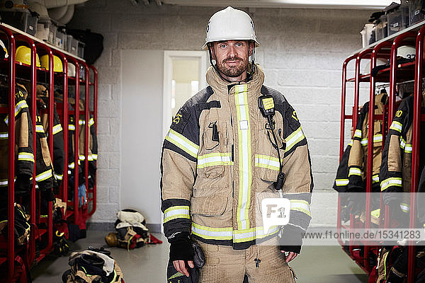 Portrait of confident male firefighter wearing protective uniform standing in locker room at fire station