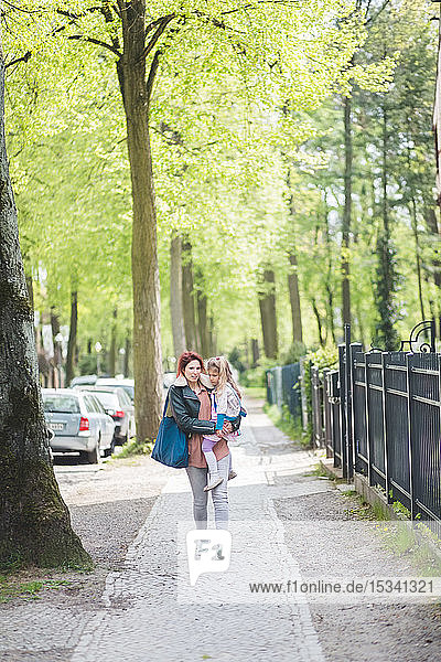 Mutter trägt Tochter in voller Länge  während sie auf einem Fußweg geht