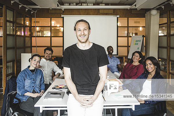 Porträt eines lächelnden Geschäftsmannes  der mit dem Team im Hintergrund im Sitzungssaal steht