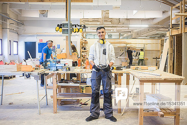 Ganzflächiges Porträt eines selbstbewussten männlichen Teenagers  der an der Werkbank eines beleuchteten Workshops steht
