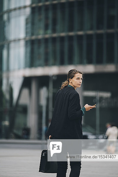 Businesswoman looking over shoulder while walking on street in city