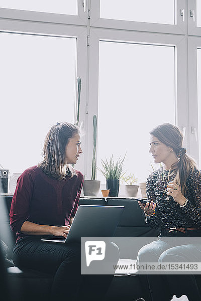 Confident female colleagues discussing while sitting in creative office