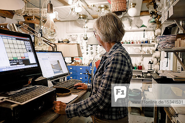 Side view of senior saleswoman using computer while standing at checkout in hardware store