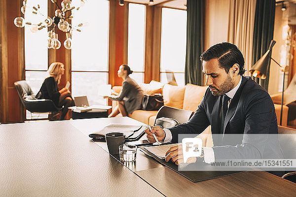 Mid adult lawyer reading documents while female colleagues discussing in background