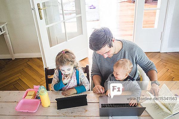 High angle view of smiling father with cute son sitting by daughter using digital tablet at table