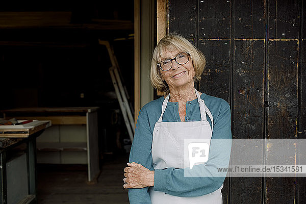Porträt eines lächelnden älteren Unternehmers  der am Eingang eines Eisenwarenladens steht