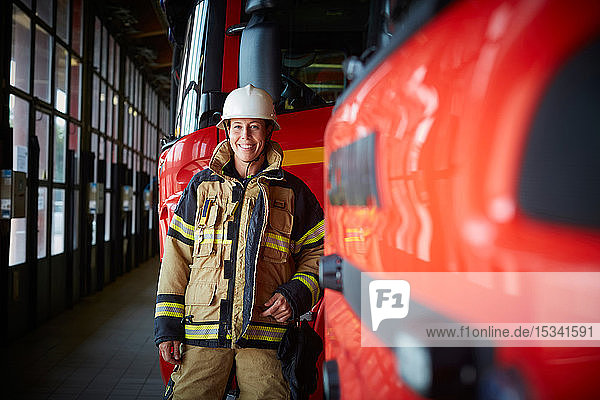 Porträt einer lächelnden Feuerwehrfrau  die in der Feuerwache beim Löschfahrzeug steht