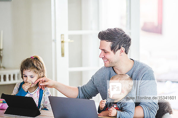 Lächelnder Vater sitzt mit seinem Sohn zusammen  während er ein Mädchen berührt  das sich zu Hause einen Film auf einem digitalen Tablet anschaut