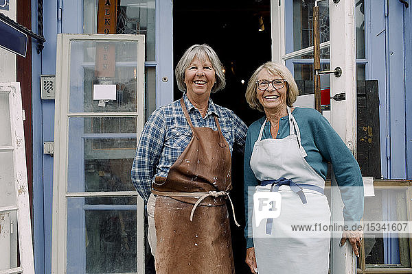 Porträt fröhlicher älterer weiblicher Mitarbeiter  die am Eingang des Geschäfts stehen