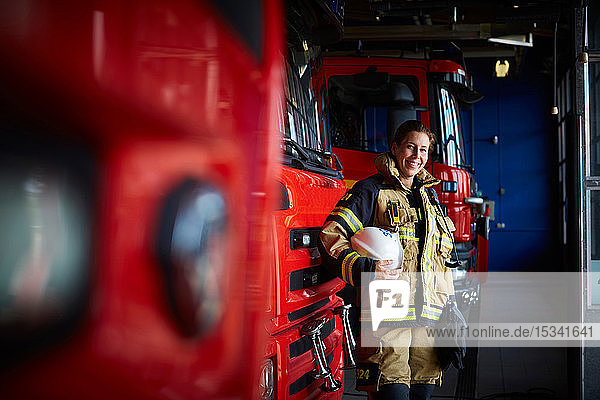 Porträt eines lächelnden Feuerwehrmannes mit Helm  der in der Feuerwache beim Löschfahrzeug steht