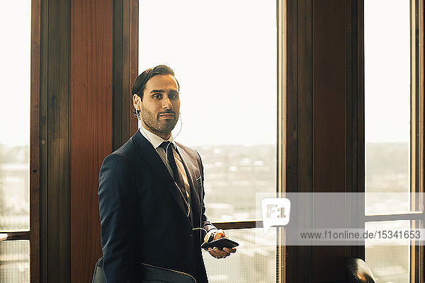 Portrait of confident financial advisor with smart phone against window at law office