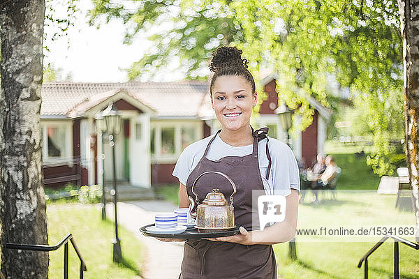 Porträt einer lächelnden jungen Kellnerin  die im Restaurant ein Serviertablett hält
