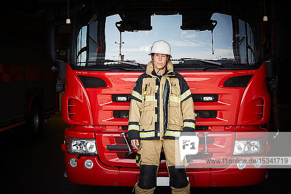 Portrait of female firefighter standing in front of fire engine at fire station