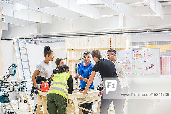 Männlicher Ausbilder unterrichtet Auszubildende  die an der Werkbank in einer beleuchteten Werkstatt stehen  über das Niveau