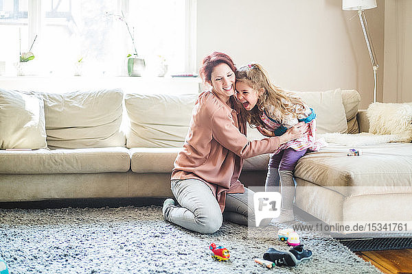Smiling woman embracing daughter sitting on sofa at home