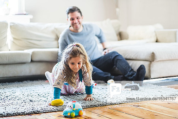 Happy man looking at daughter playing with toys at home