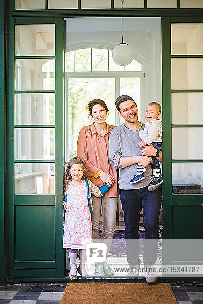 Ganzflächiges Porträt einer lächelnden Familie  die am Hauseingang steht