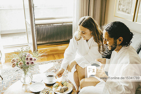 Hochwinkelansicht eines Paares im Bademantel beim Frühstück im Hotelzimmer
