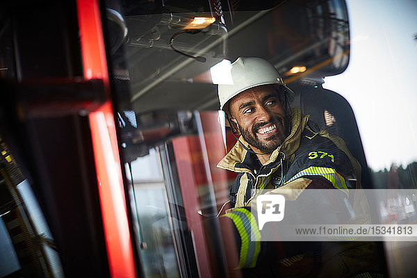 Lächelnder Feuerwehrmann im Feuerwehrauto sitzend durch Glasfenster gesehen