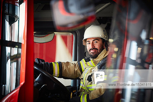 Portrait of confident male firefighter sitting in fire engine at fire station